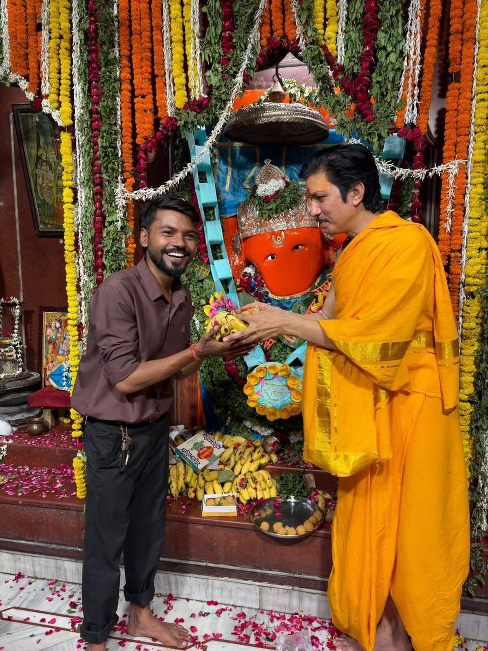 Aman Prajapati, in a coffee-coloured shirt, with Acharya Neelesh Pandey Ji before the Hanuman ji murti