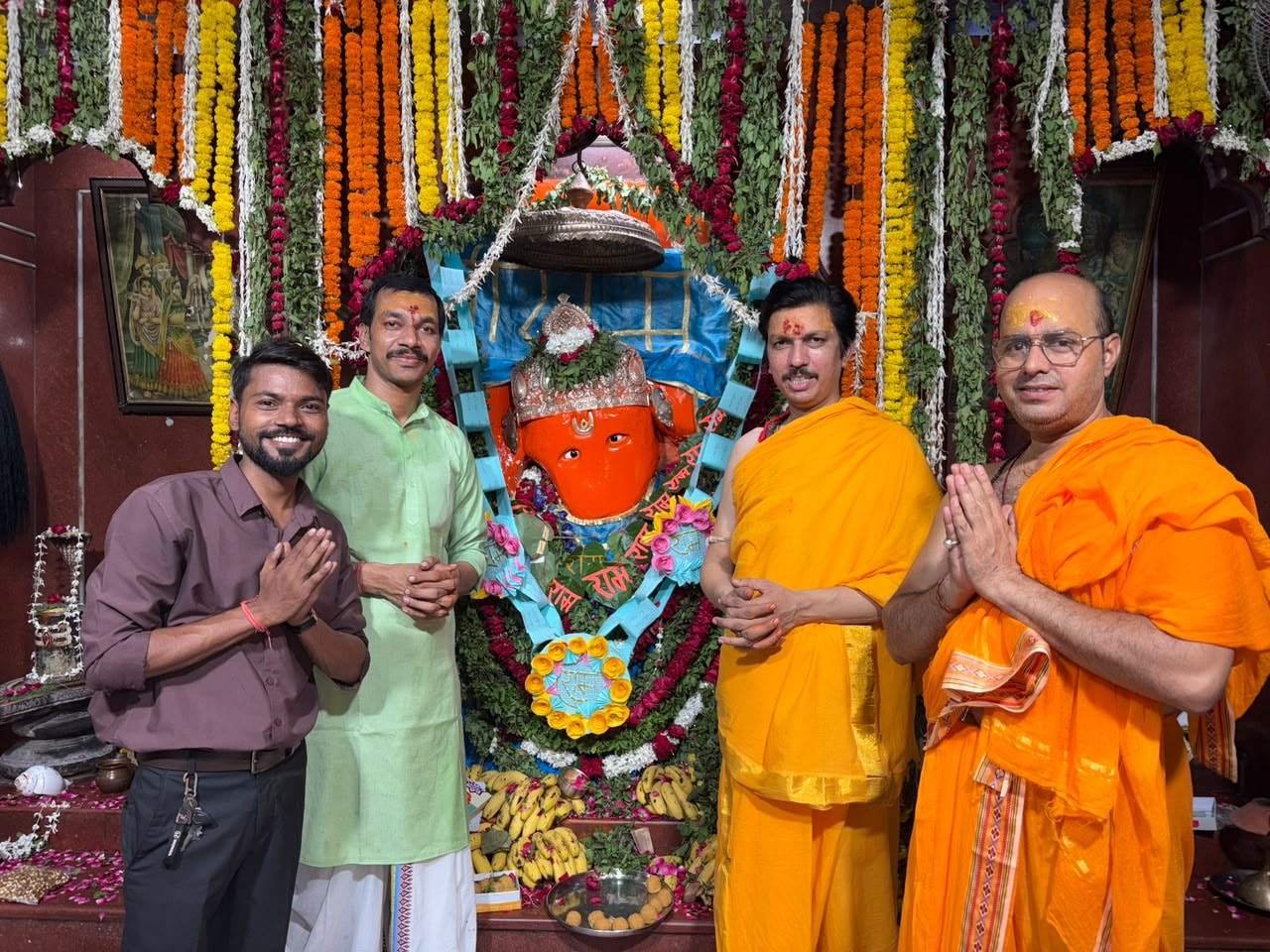 Four people standing together before the flower-adorned Hanuman ji murti at the temple